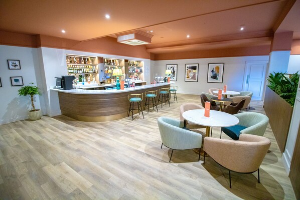 Una zona de bar con barra, taburetes y una sala de estar con mesas redondas y sillas.