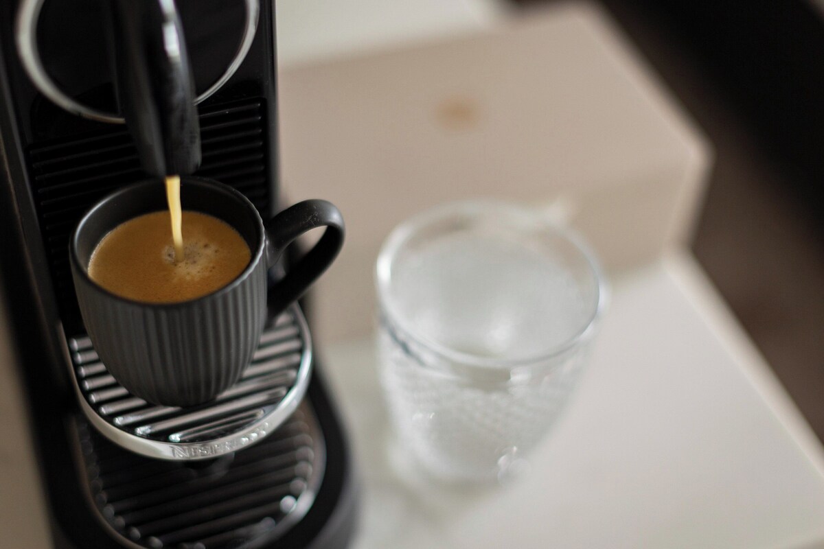 A coffee machine dispensing coffee into a cup, a glass of water, and a white surface.