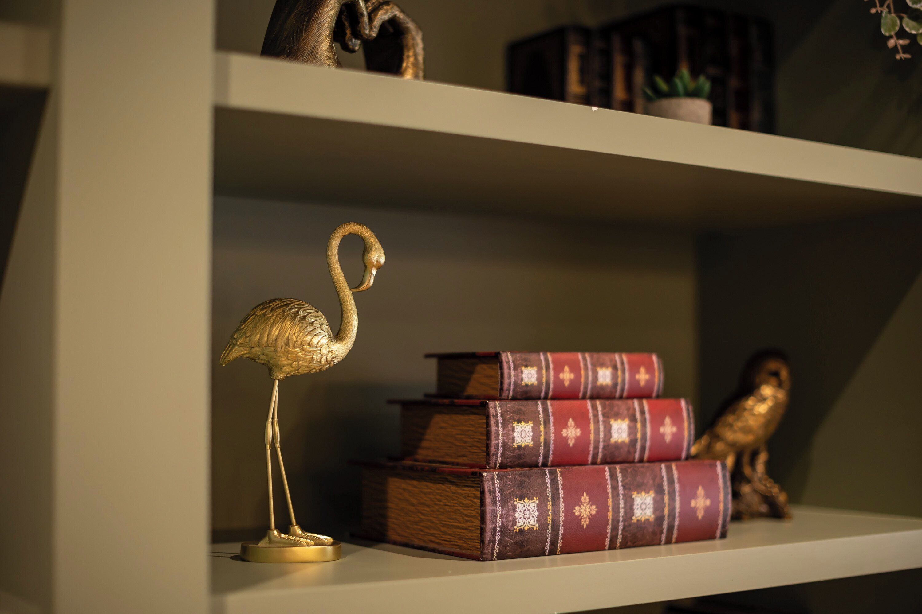 A bookshelf with decorative items including a golden flamingo, stacked books, and a small owl figurine.
