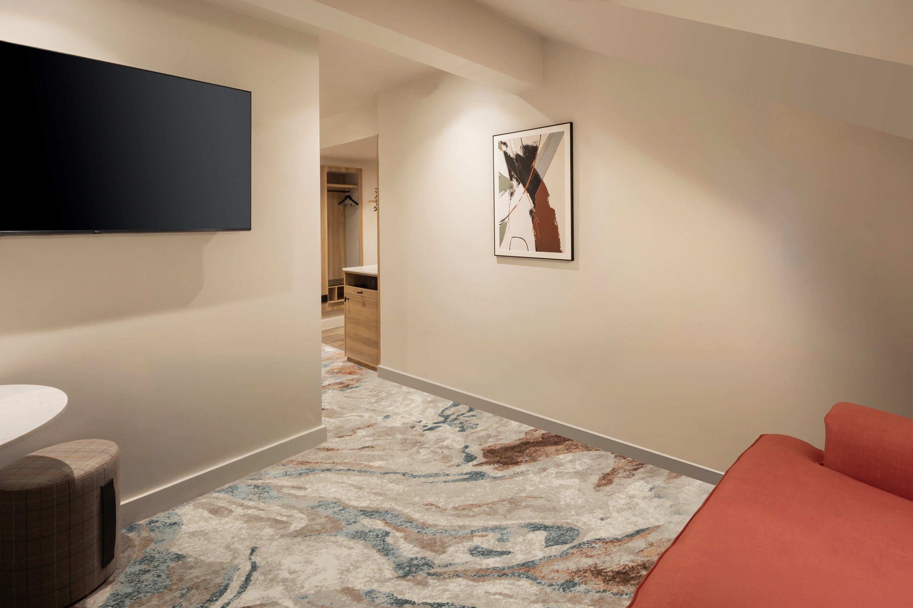 A hallway with a modern design, a flat-screen TV mounted on the wall, a patterned carpet, and a red upholstered bench.