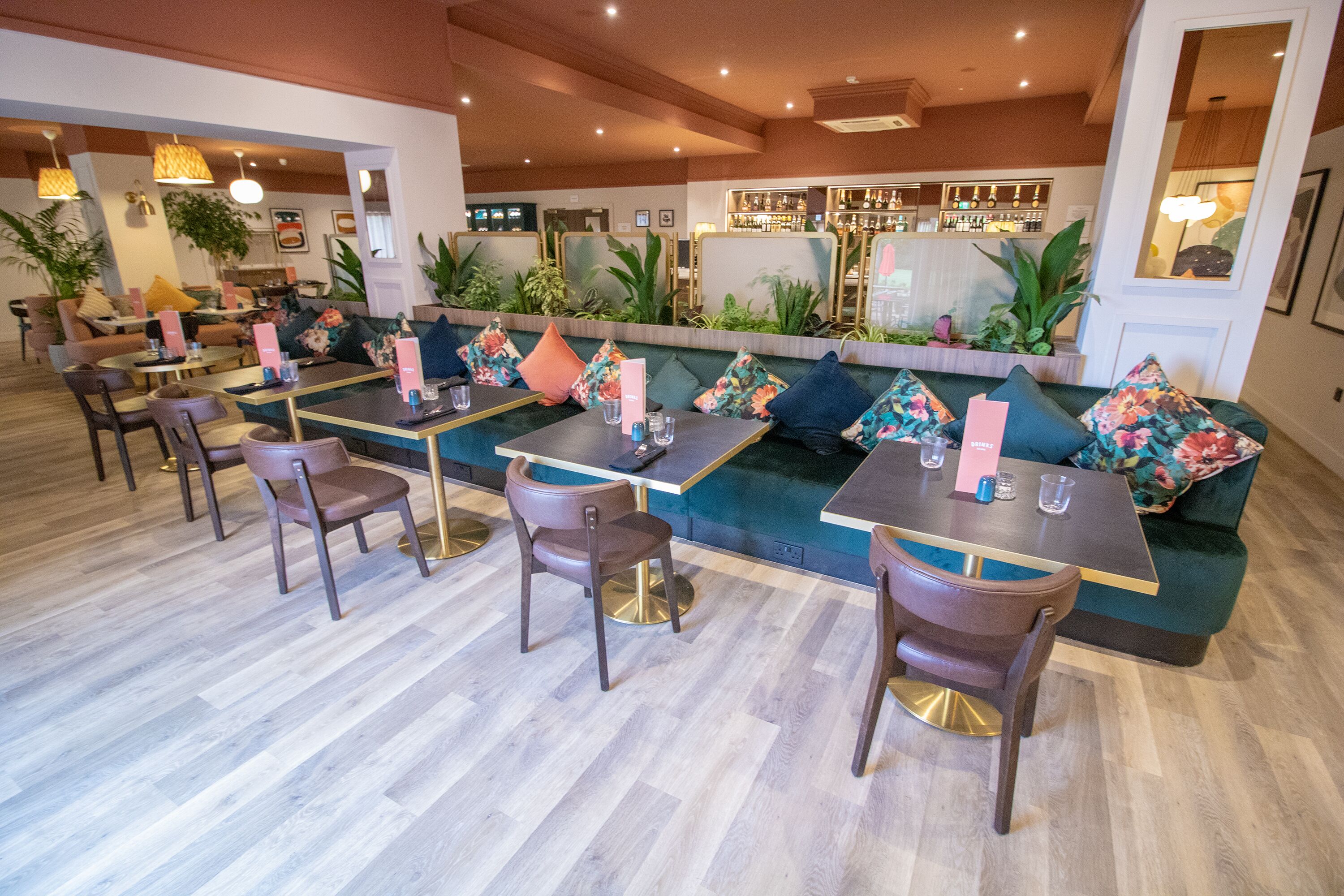 A modern restaurant with a bar area, wooden flooring, and green upholstered seating.