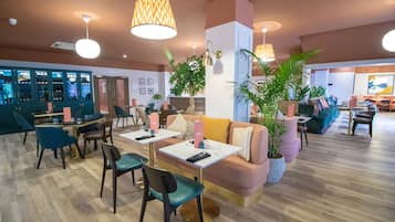 Un hall d’hôtel moderne doté d’un bar, de différents espaces de détente et de plantes décoratives.