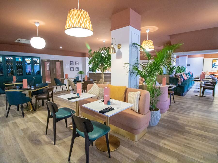 Un hall d’hôtel moderne doté d’un bar, de différents espaces de détente et de plantes décoratives.