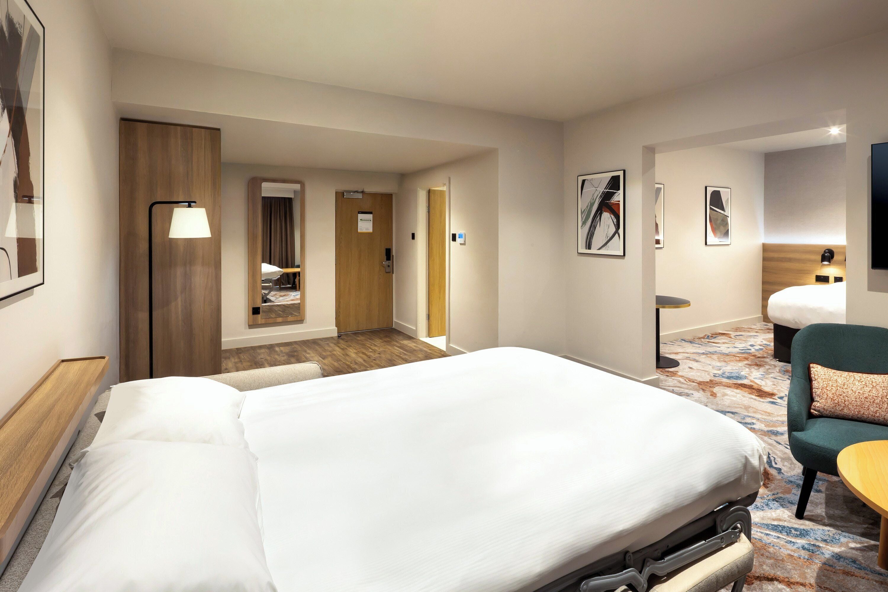 A hotel room with a large bed, a desk, a chair, a lamp, and a bathroom.