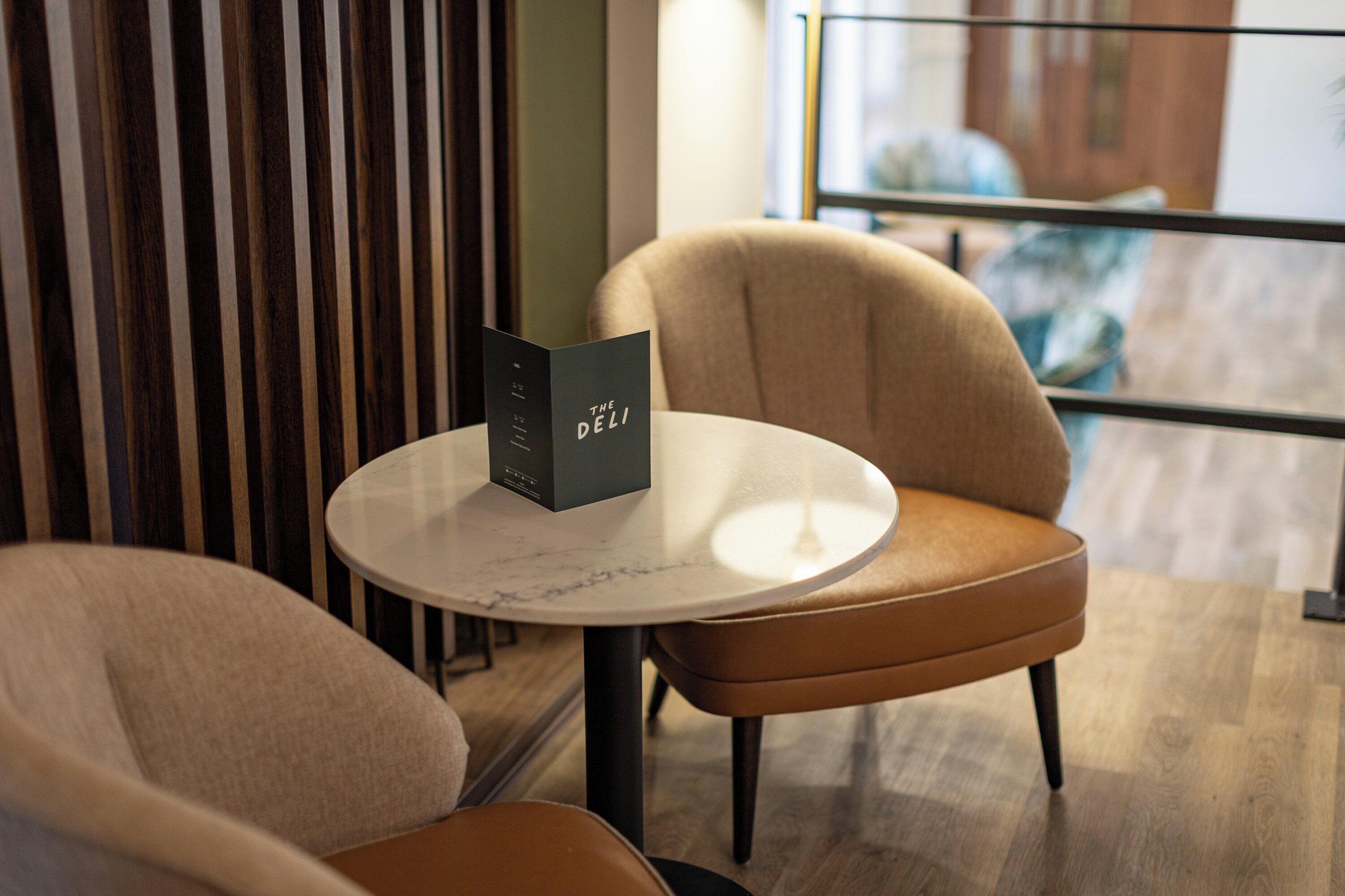A modern interior with a round table, two chairs, and a menu stand.