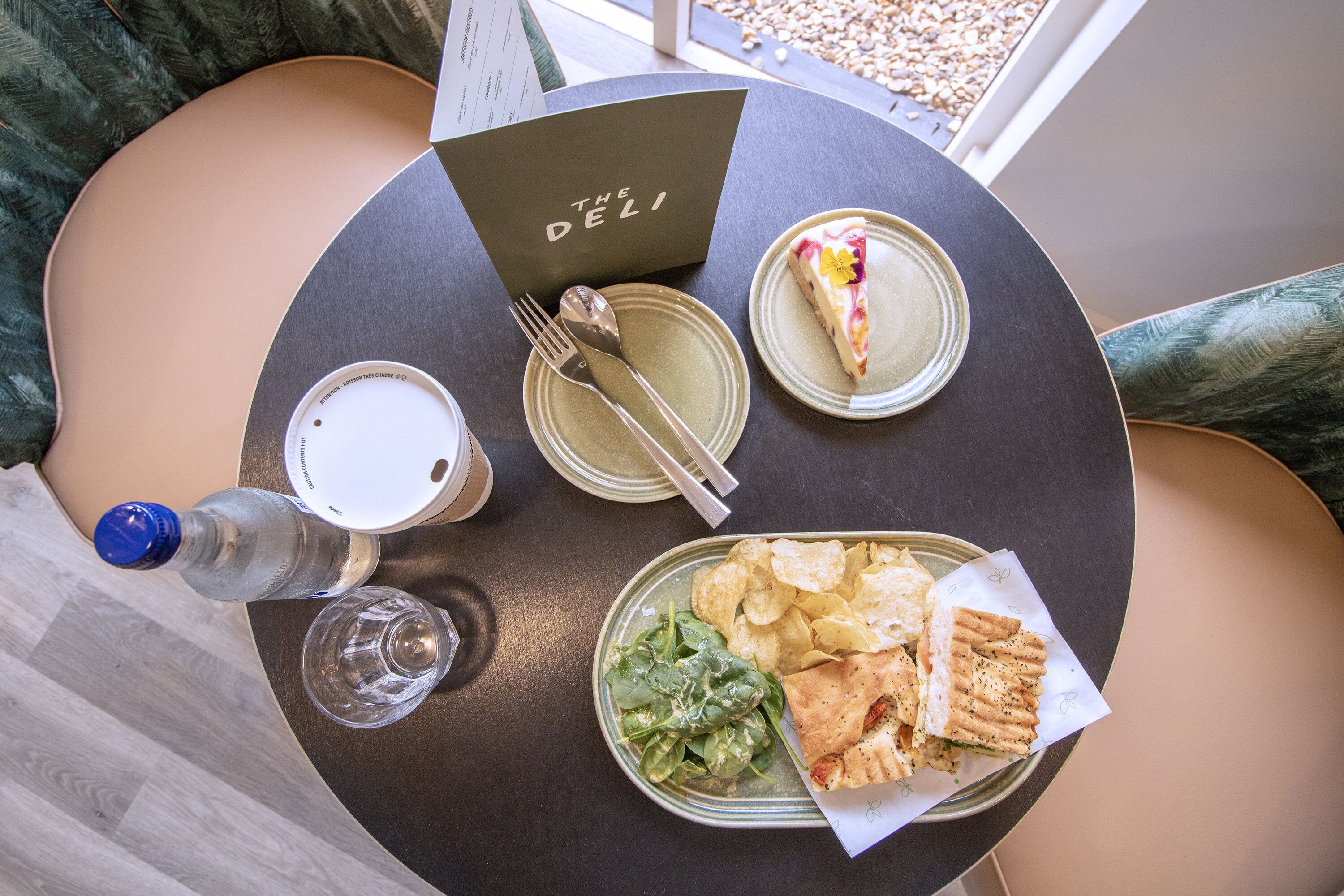 Una mesa con un menú, una porción de pizza, un plato de papas fritas, un sándwich y una botella de agua.
