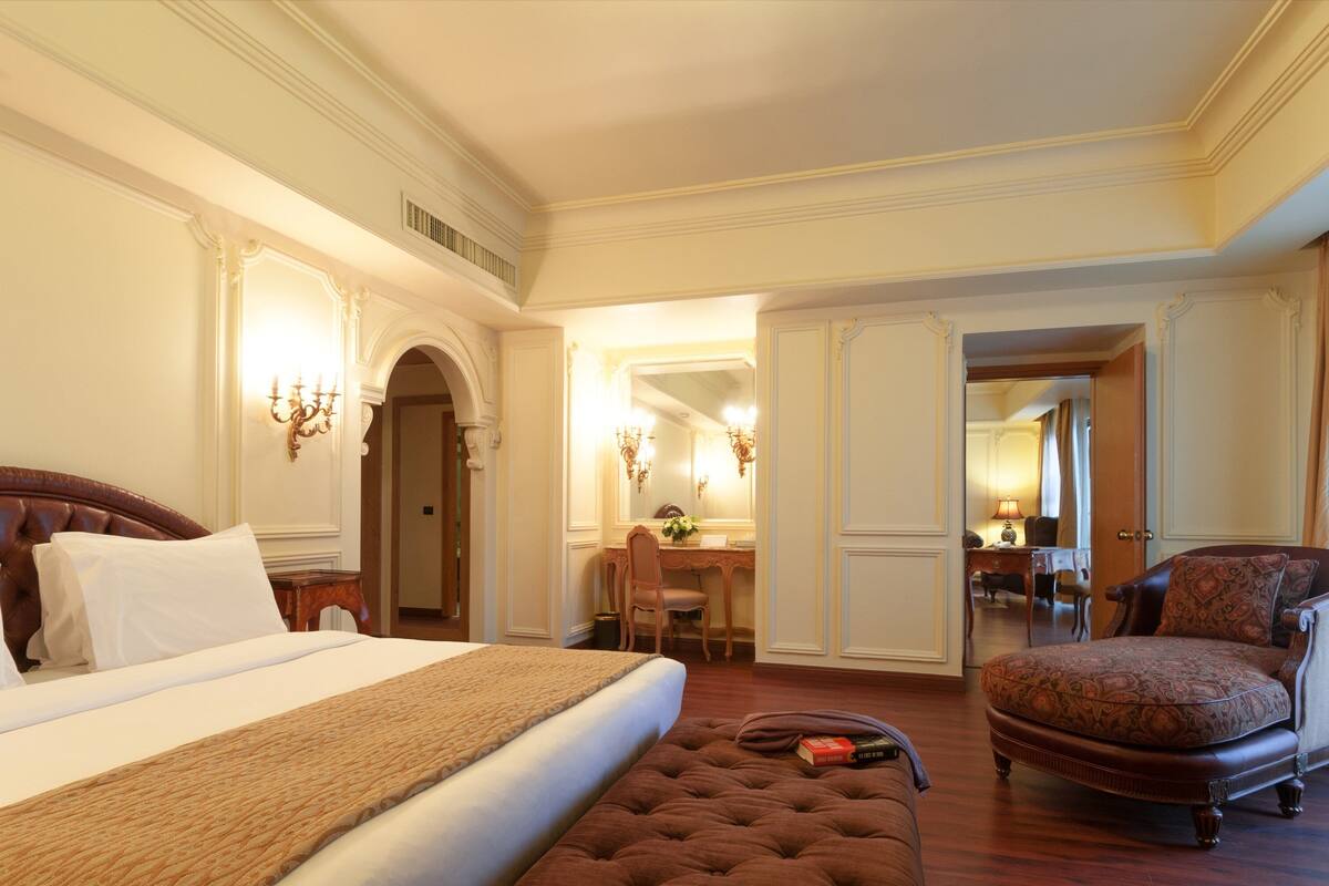 A hotel room with a large bed, a sitting area with a chair, a desk, and a mirror.
