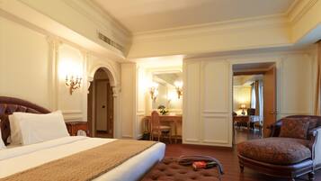 A hotel room with a large bed, a sitting area with a chair, a desk, and a mirror.