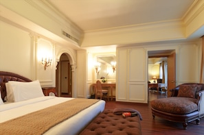 A hotel room with a large bed, a sitting area with a chair, a desk, and a mirror.