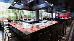 A modern restaurant with a long counter, bar seating, and a view of greenery outside. - Le Commodore (Beirut)