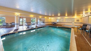 An indoor swimming pool with clear water, surrounded by lounge chairs and tables, and a tiled floor. - Fairfield Inn by Marriott Battle Creek (Battle Creek)