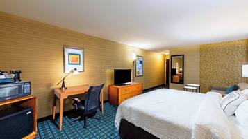Habitación de hotel con cama, escritorio, silla, televisor y una pequeña mesa.