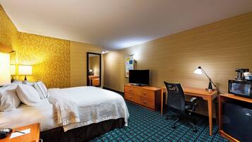 A hotel room with a bed, a desk with a chair, a television, and a desk lamp.