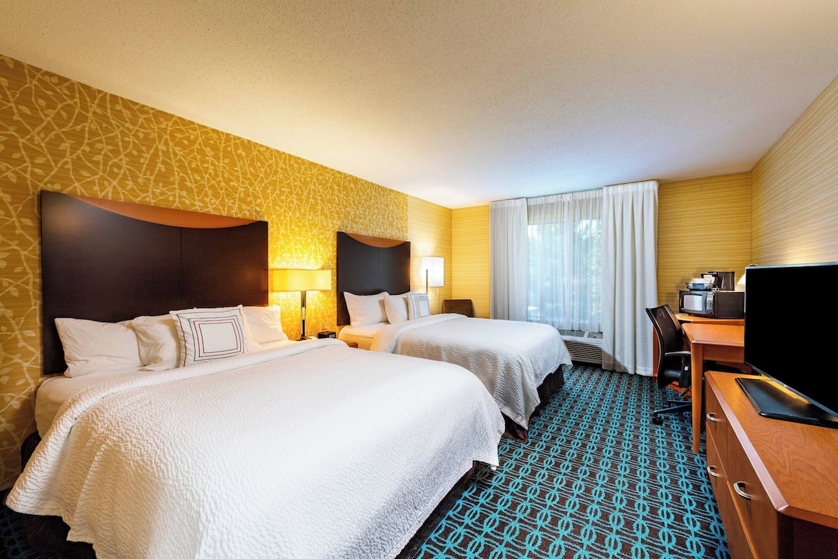 A hotel room with two beds, a desk with a TV, and a window with curtains.