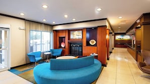 A hotel lobby with a curved blue sofa, a fireplace, and a dining area. - Fairfield Inn by Marriott Battle Creek (Battle Creek)
