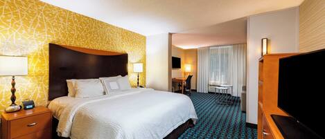Une chambre d’hôtel avec un grand lit, des tables de chevet, un bureau, une chaise, une télévision et une moquette à motifs.