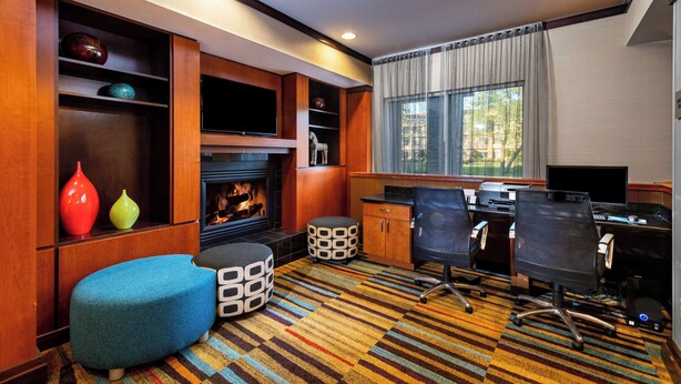 A modern hotel room with a fireplace, a desk with two chairs, a large window with curtains, and a colorful striped carpet. - Fairfield Inn by Marriott Battle Creek (Battle Creek)