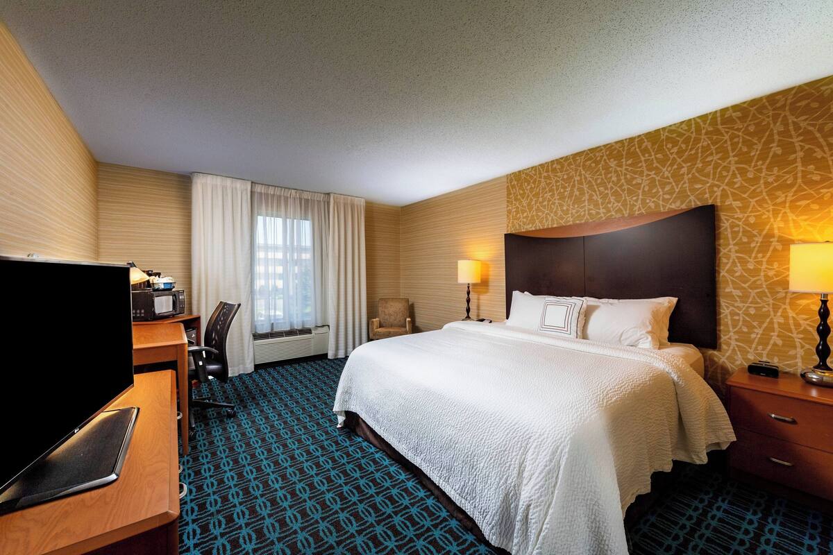 A hotel room with a bed, desk, chair, TV, and lamps.