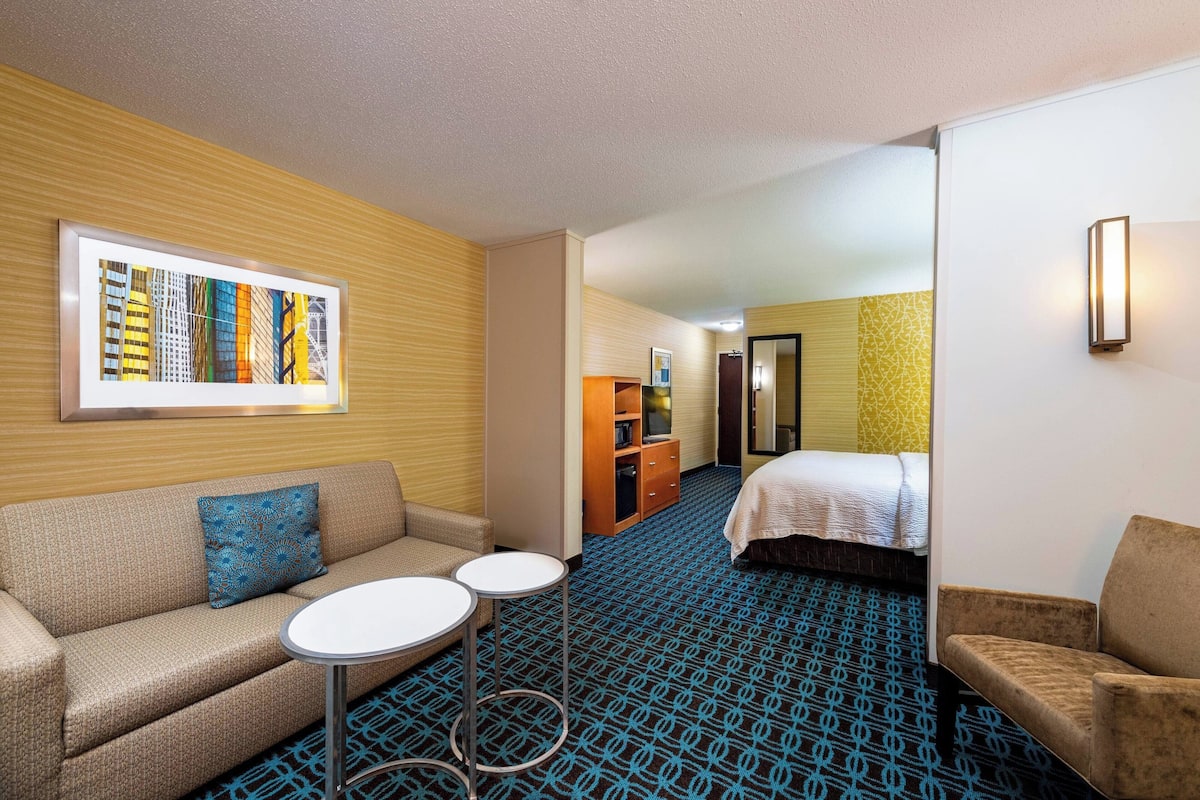 A hotel room with a sofa, two small tables, a bed, and a hallway leading to a bathroom.
