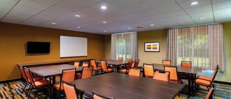 A conference room with a large table, multiple chairs, a projector screen, and a carpeted floor.
