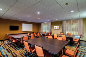 A conference room with a large table, multiple chairs, a projector screen, and a carpeted floor.