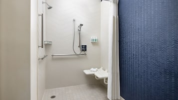 A shower area with a white tiled floor, a showerhead, a handheld shower, and a small shelf with toiletries.