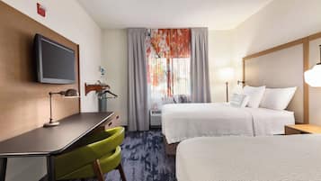 Una habitación de hotel con cama, escritorio y silla, televisor y ventana con cortinas.