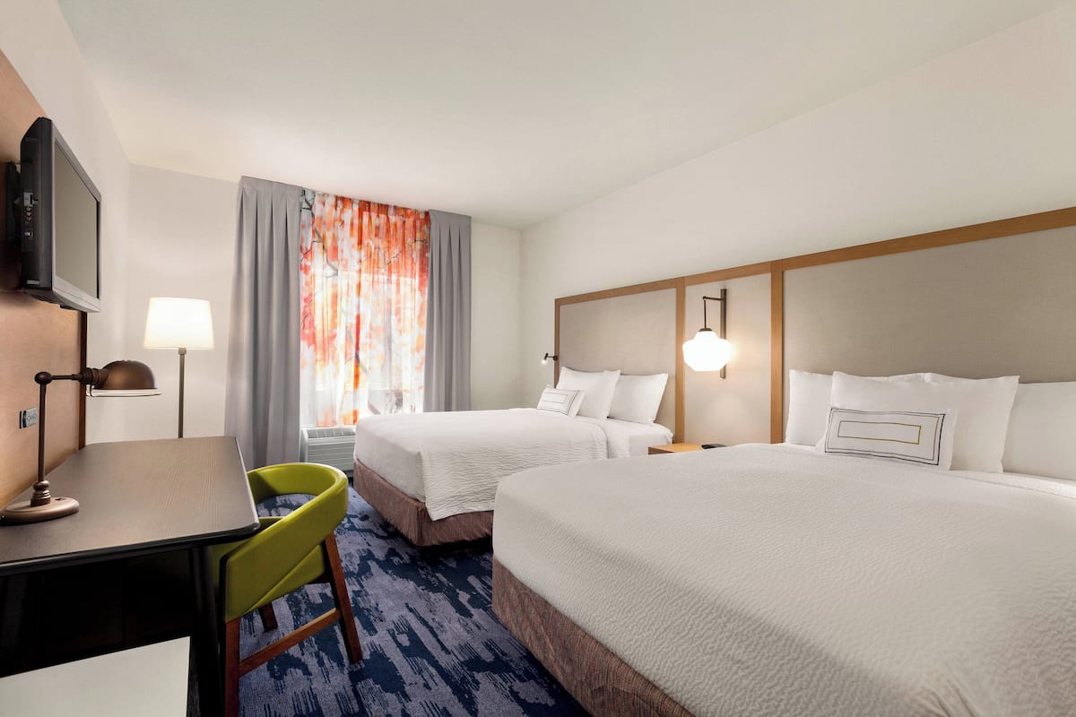 A hotel room with two beds, a desk, a chair, a television, and a window with curtains.
