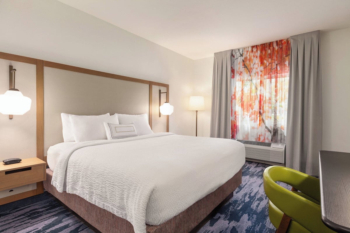 A hotel room with a large bed, bedside lamps, a desk, and a chair.