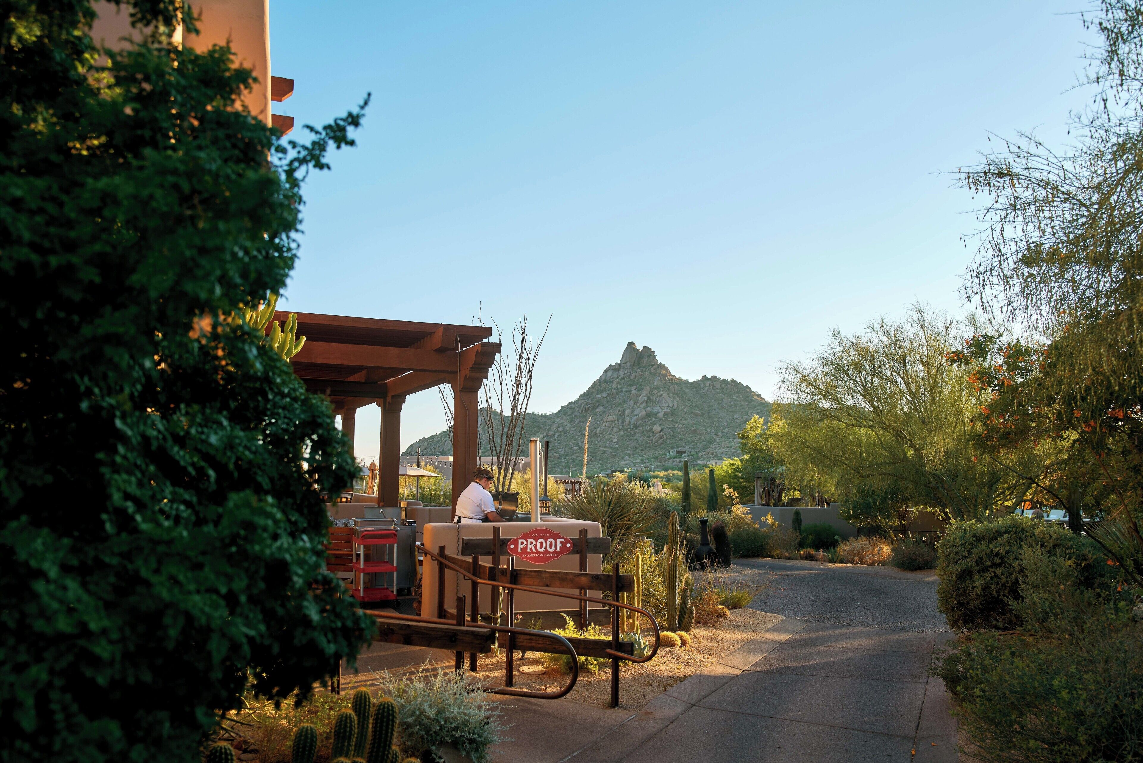 A desert-themed outdoor seating area with a 'PROOF' sign, cacti, and a mountain in the background.