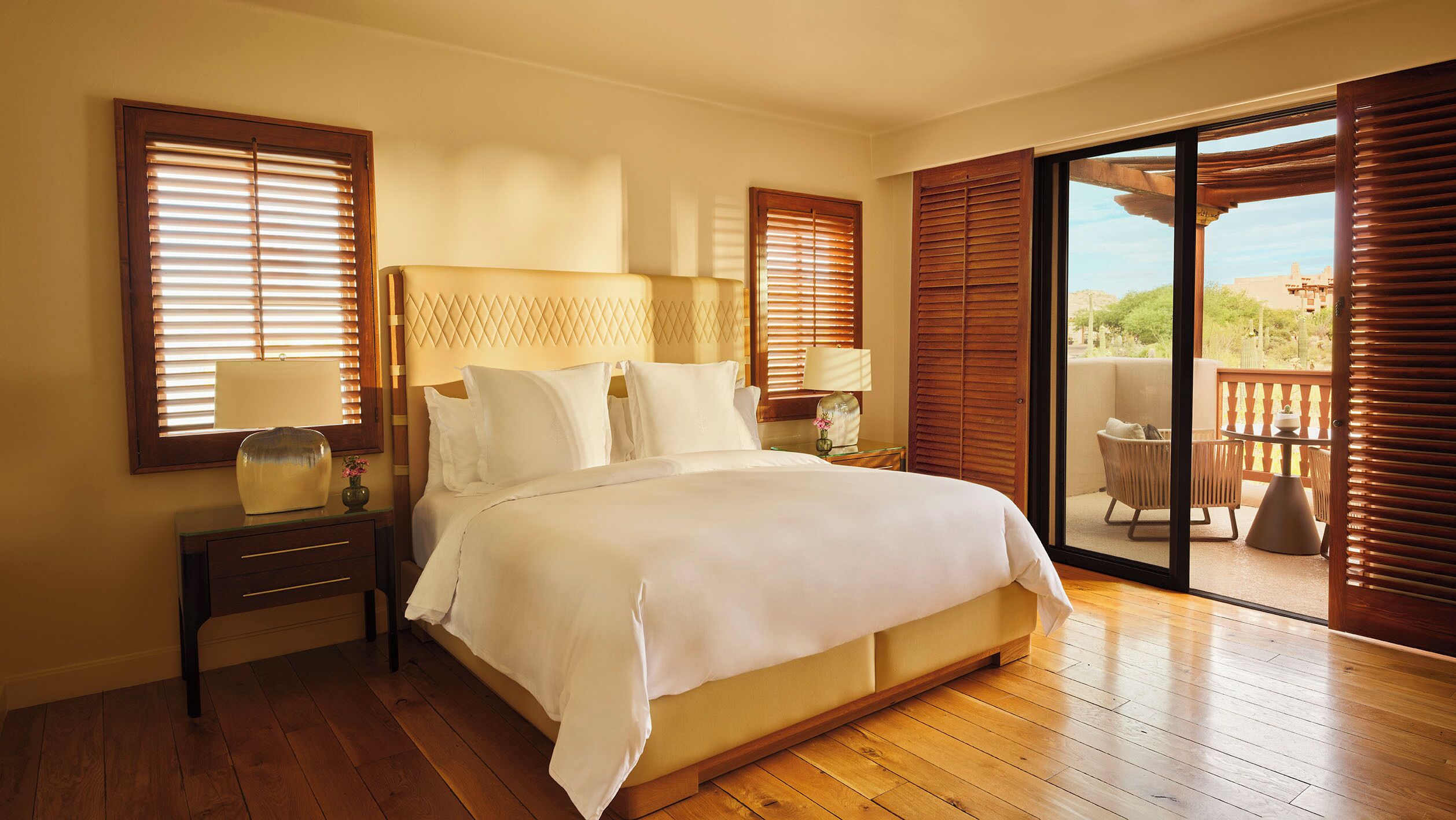 Un dormitorio amplio con una cama grande, suelo de madera y un balcón con mobiliario exterior.