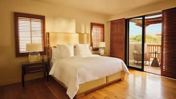 Un dormitorio amplio con una cama grande, suelo de madera y un balcón con mobiliario exterior.