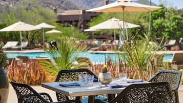 An outdoor dining area with wicker chairs and a table, overlooking a pool and mountains.