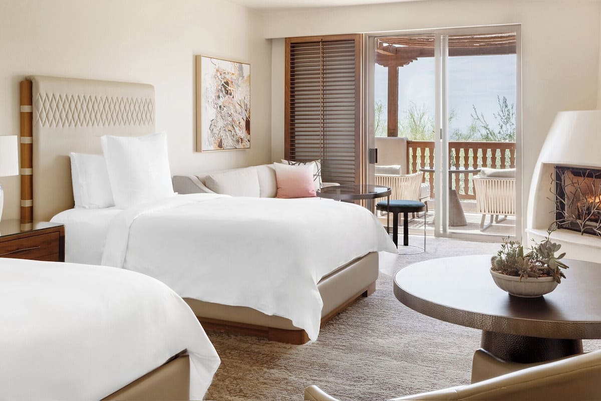 Een hotelkamer met twee bedden, een balkon met zitplaatsen buiten, en een open haard.
