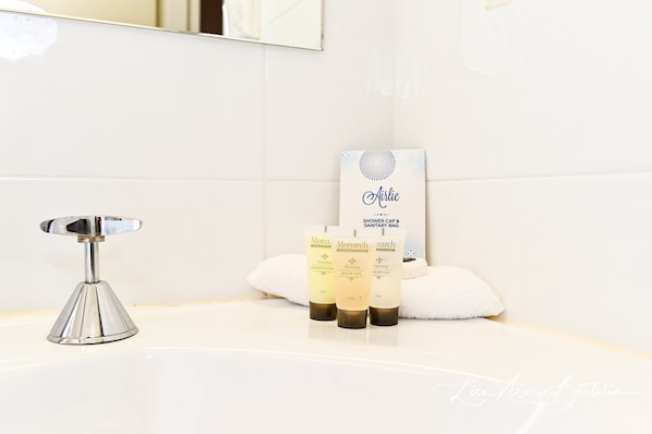 Un baño con un lavamanos blanco, un grifo cromado y tres botellas de productos de la marca Monarch.
