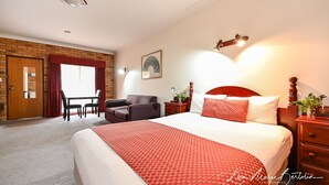 A hotel room with a large bed, a desk with a chair, a small table, and a red and white patterned bedspread.
