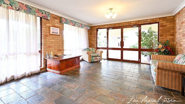 A spacious room with a brick wall, a wooden cabinet, a wicker sofa, and a large window with curtains.