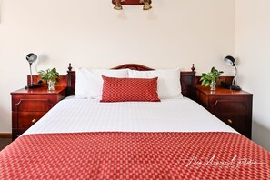 A neatly made bed with a checkered red and white bedspread, two bedside tables with lamps, and a wall-mounted light fixture.