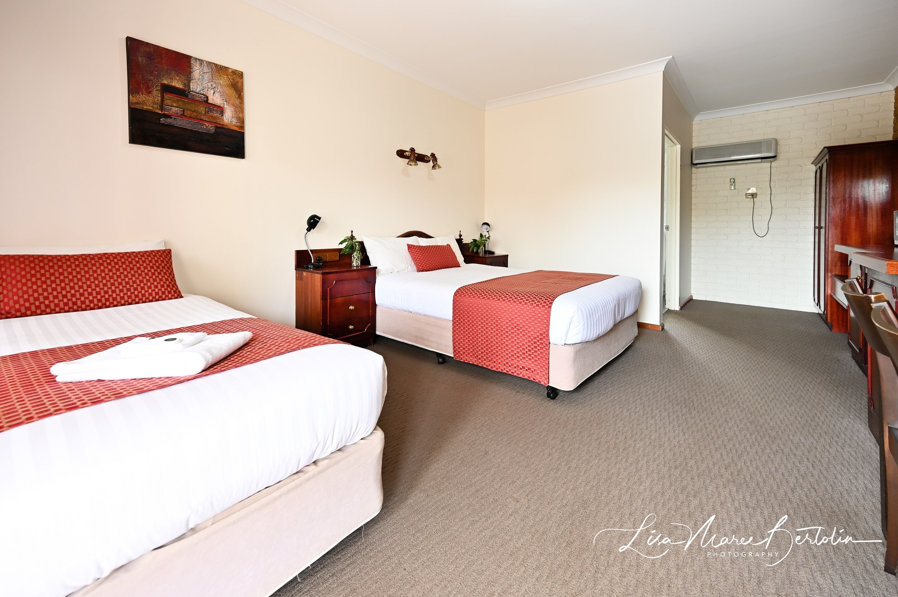 A hotel room with two beds, a wardrobe, a shower, and a painting on the wall.