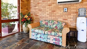 A room with a brick wall, a floral-patterned sofa, a large potted plant, and a water dispenser.