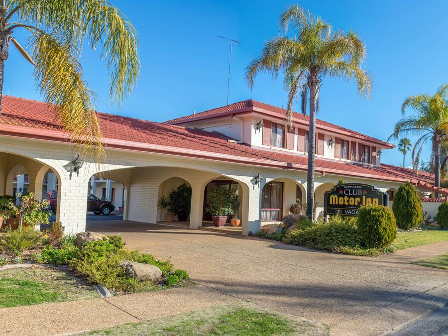 Un bâtiment à deux étages, doté d’un toit recouvert de tuiles rouges, d’un patio abrité et d’une enseigne indiquant « NARRANDERA CLUB Motor Inn ».