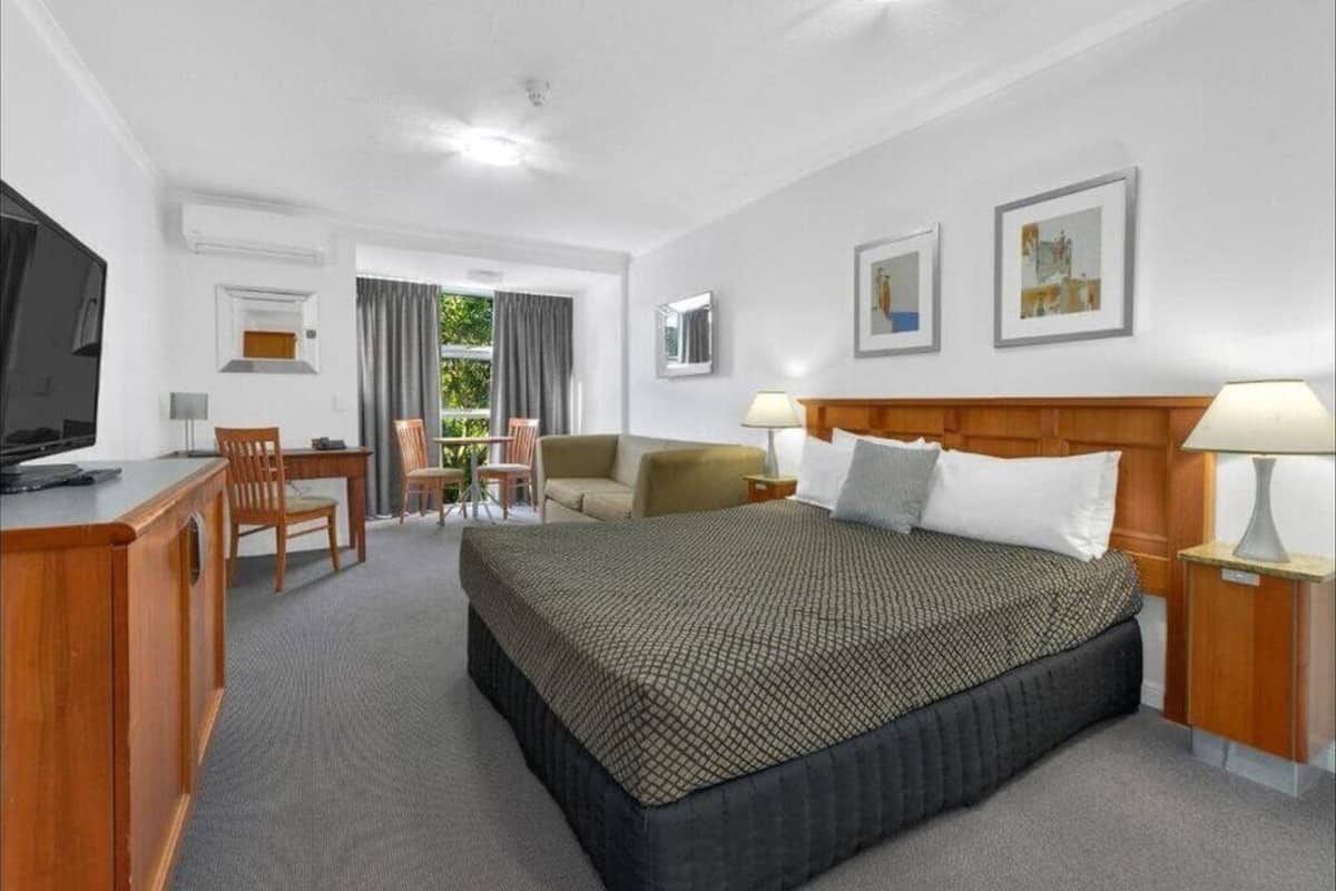 Ein Hotelzimmer mit Bett, Schreibtisch, Stuhl, Fernseher und einem Fenster mit Vorhängen.