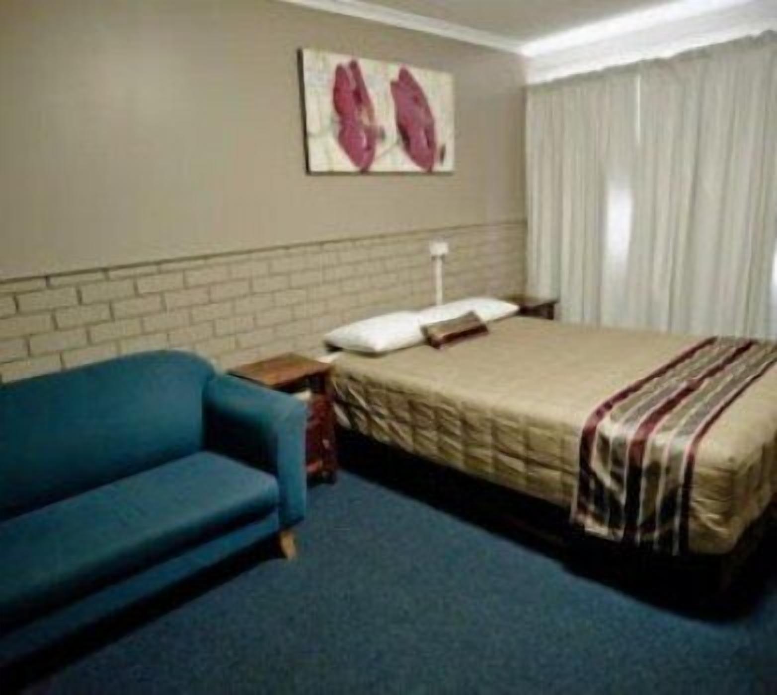 A hotel room with a bed, a blue sofa, a brick wall, and a painting on the wall.