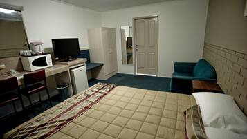 Una habitación de hotel con cama, escritorio con computadora, microondas y televisión.
