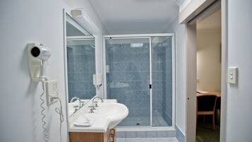 Un baño con cabina de ducha de vidrio, un lavabo blanco y un secador de pelo montado en la pared.