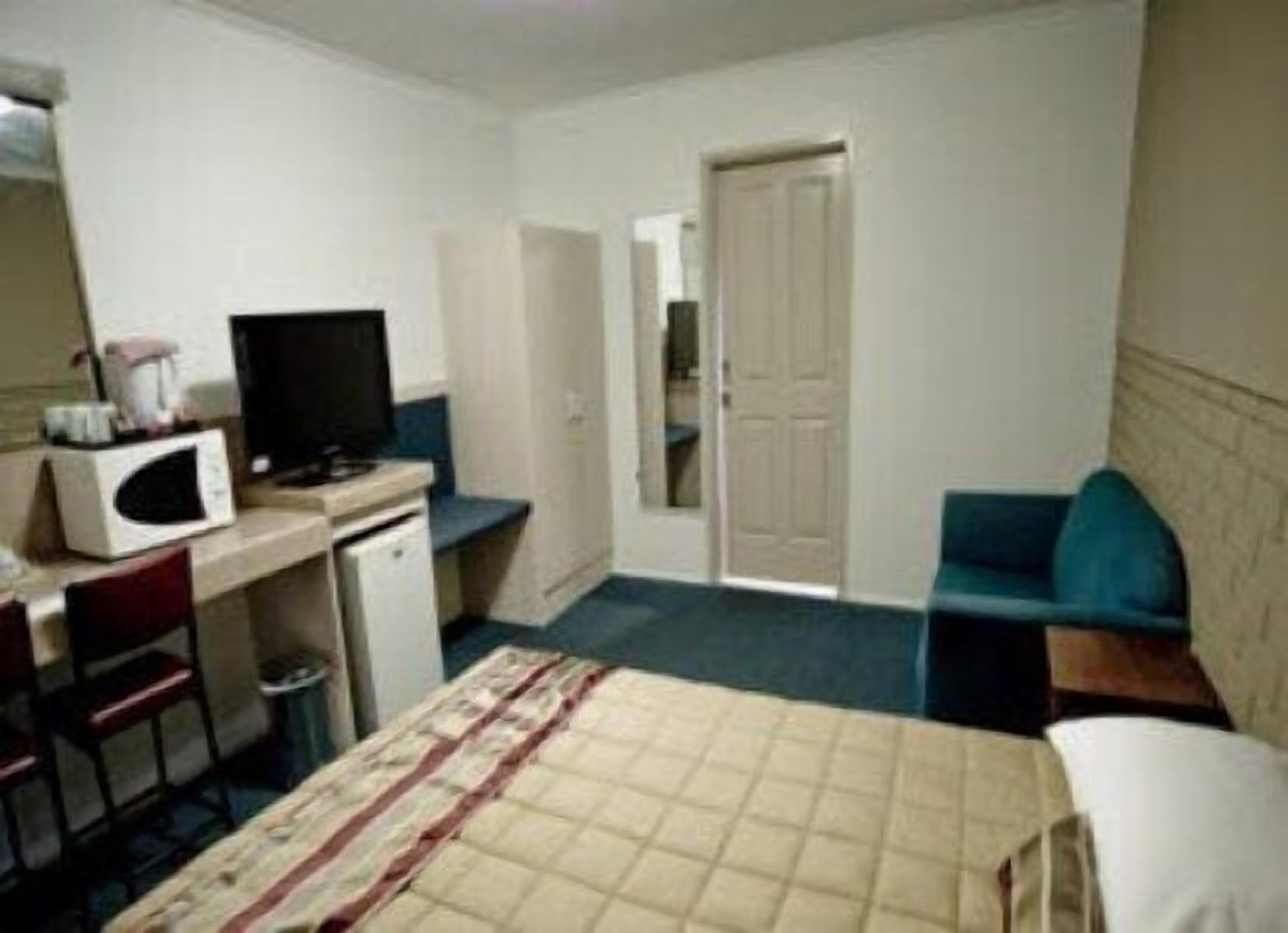 Une petite chambre d’hôtel simple, comprenant un lit, un bureau avec un ordinateur, une chaise, une télévision et une porte donnant sur une autre pièce.