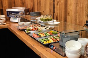 A buffet with various fruits and dishes, a digital scale, and stacked plates.