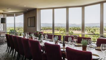 A dining area with a table set for six, large windows, and a view of a vineyard.
