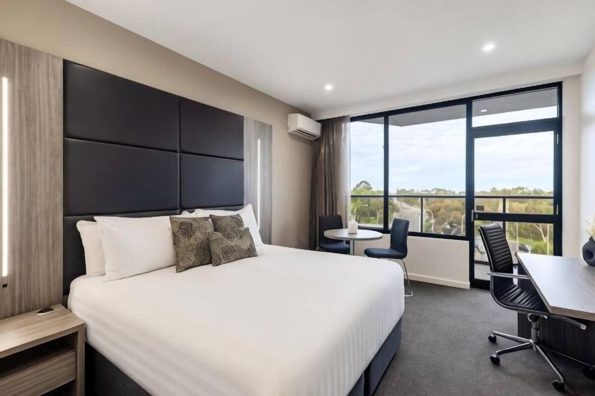A hotel room with a large bed, a desk, a chair, and a view of the outdoors.