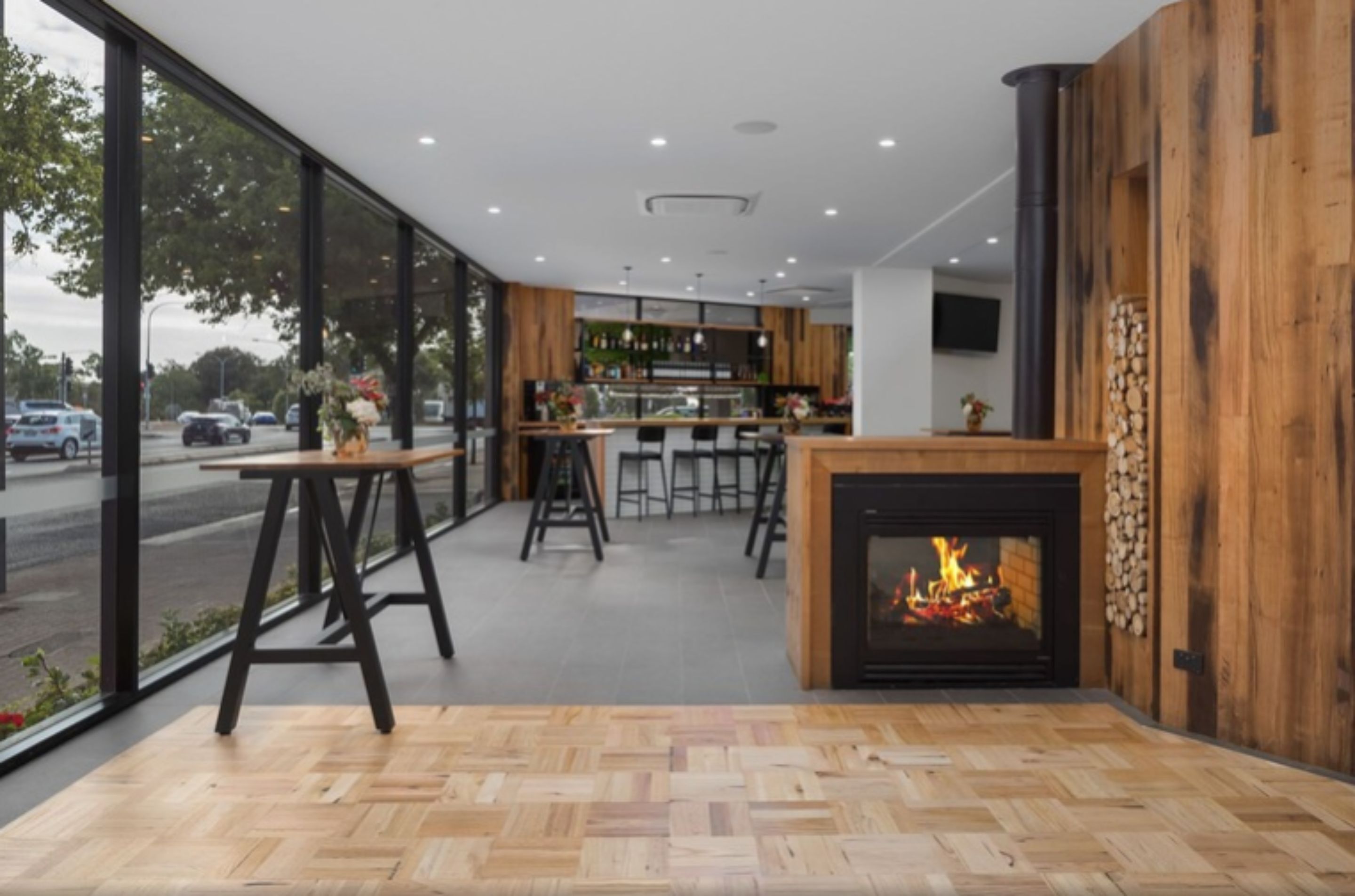 Un intérieur moderne avec une cheminée, un plancher en bois et de grandes fenêtres donnant sur la rue.